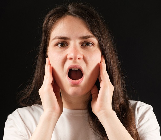 Woman holding her jaw on both sides of her head